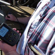 Close-up of a person in a plaid shirt using a handheld laser distance meter on a construction site