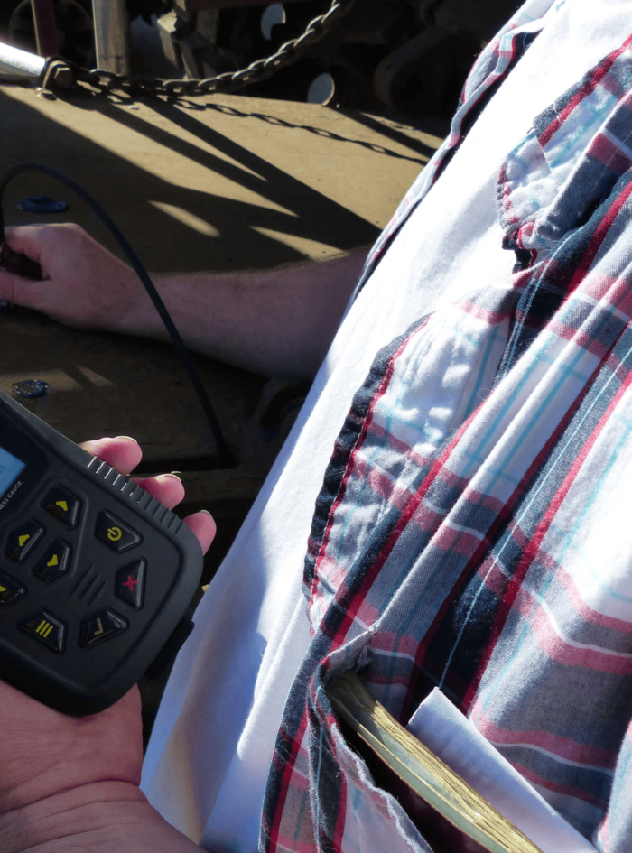 Close-up of a person in a plaid shirt using a handheld laser distance meter on a construction site
